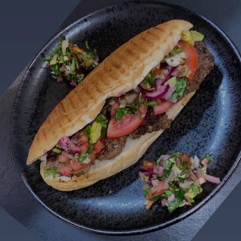 Gefuelltes Sandwich mit Fleisch Tomaten roten Zwiebeln und Kraeutern auf schwarzem Teller