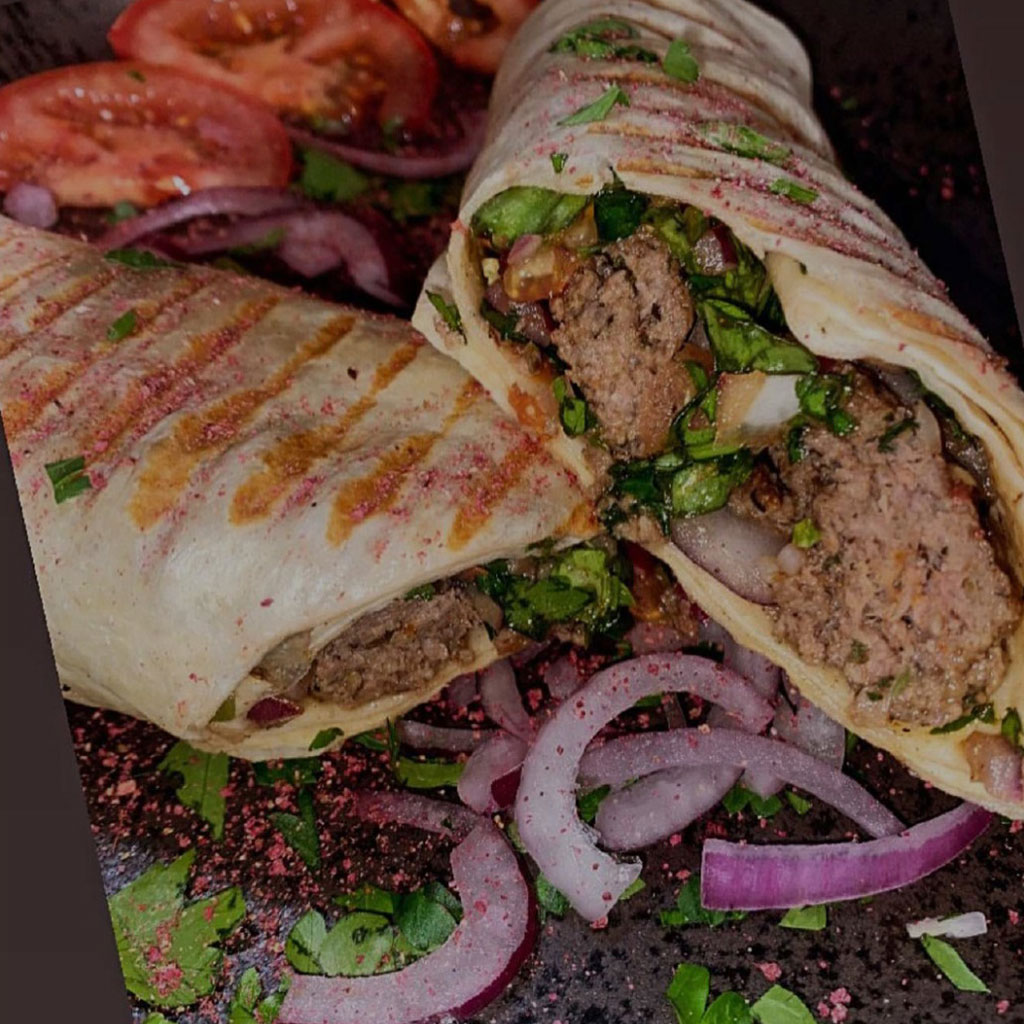 Gegrillter Wrap mit Hackfleisch und Kraeutern neben Tomaten und Zwiebeln